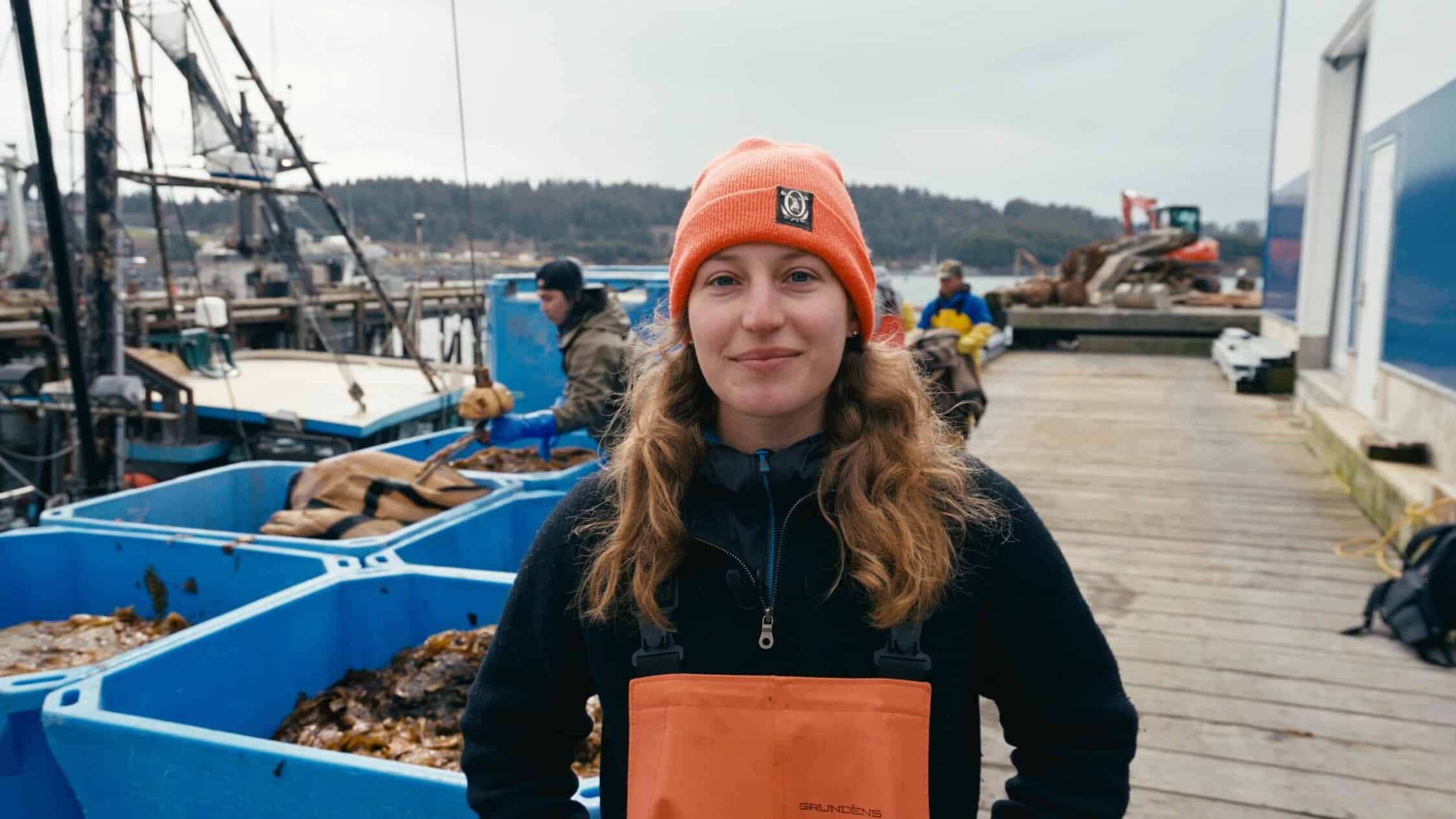 A woman wearing an orange hat and an orange jacket standing on a dock.