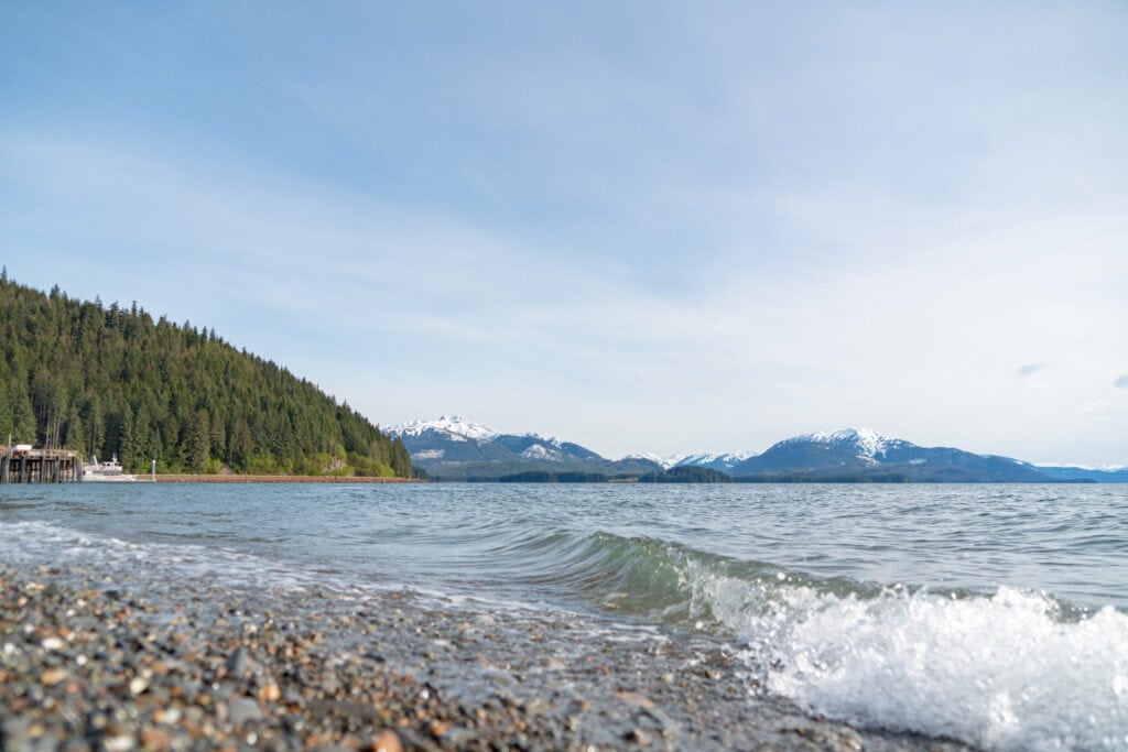 A beach with waves and mountains in the background.