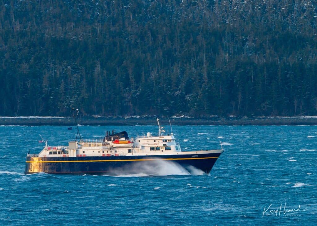 A ferry going through the water, with a mountain in the background.